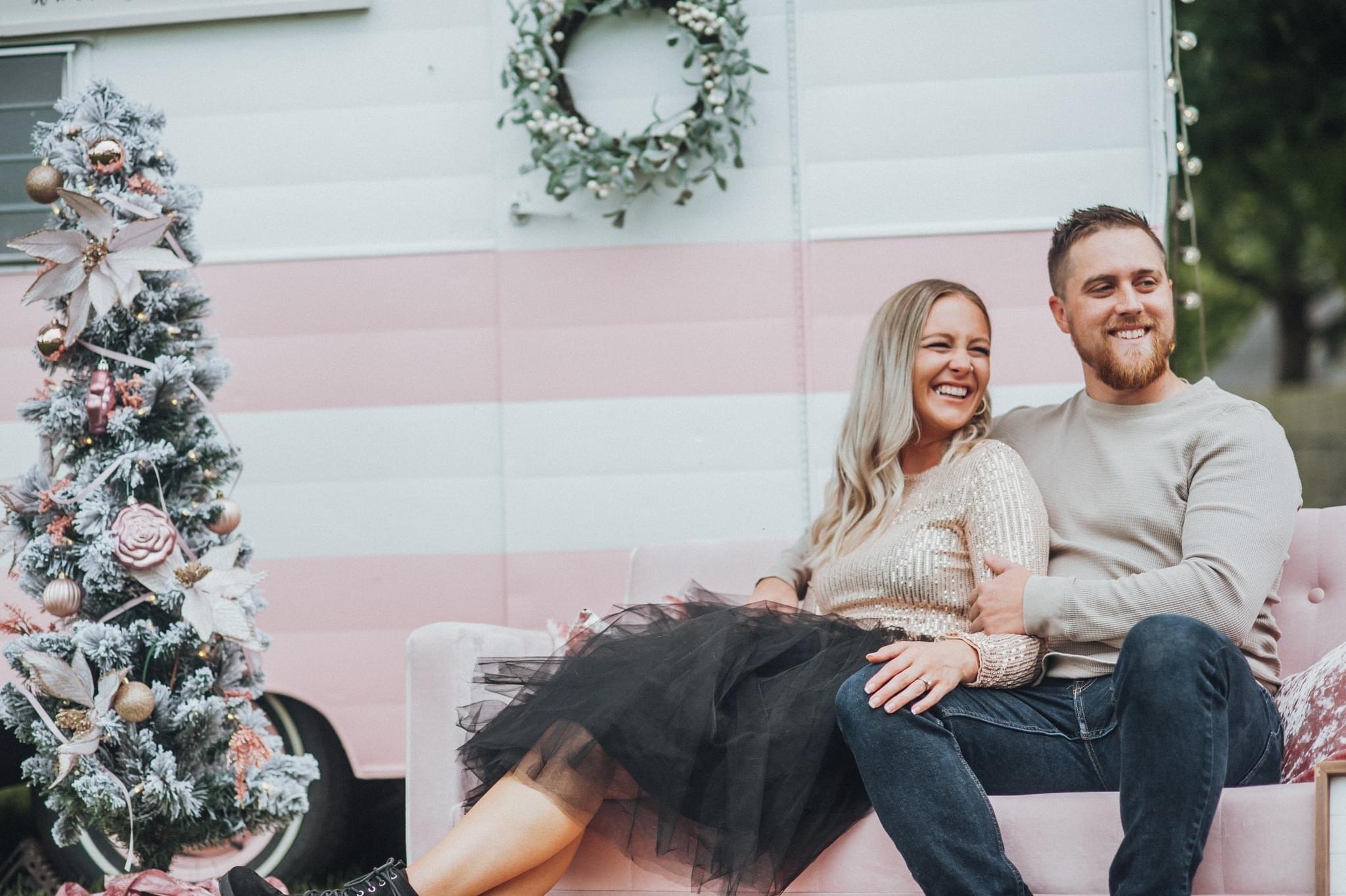 Liz laughing beside a flocked Christmas tree and a pink vintage camper decorated for the holidays